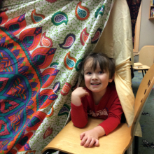 Little boy peeking out from fort.